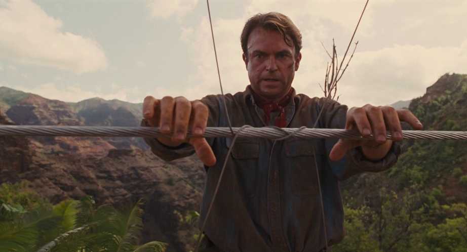 What Is Plot In Film? Definition & Examples 2 Dr. Alan Grant holds a thick steel cable with both hands, staring ahead with a tense expression, with rocky hills and jungle behind him.