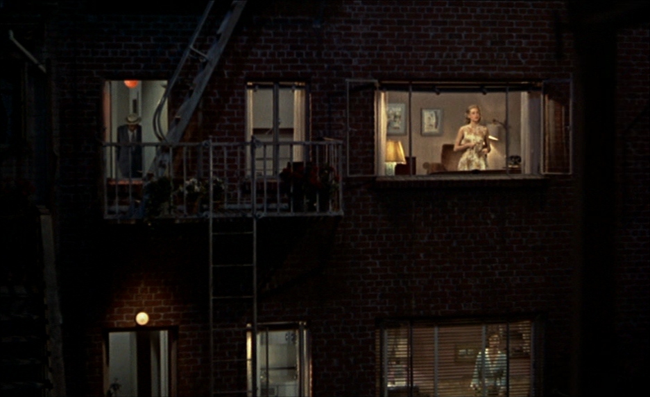 Style in Film: Auteur, Genre, and Film Movements Explained 2 Night view of an apartment building courtyard with several lit windows; a woman stands in a bright window holding something while darker windows and a fire escape frame the scene.