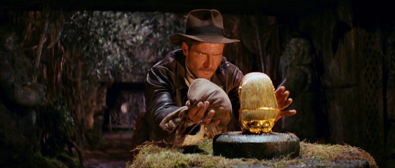 What is an Action Movie? Definition, Conventions, and Writing Tips 5 Indiana Jones reaches toward a golden idol inside a jungle temple, carefully swapping it with a sandbag to avoid triggering traps.