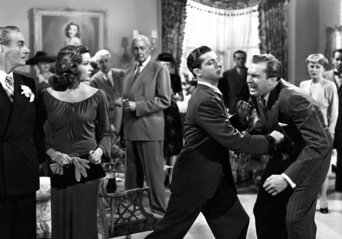 Best Mystery Movies of All Time: 25 Picks Explained 8 Black-and-white scene in a crowded room where a man restrains another man while a woman in an evening dress watches; several people stand in the background.