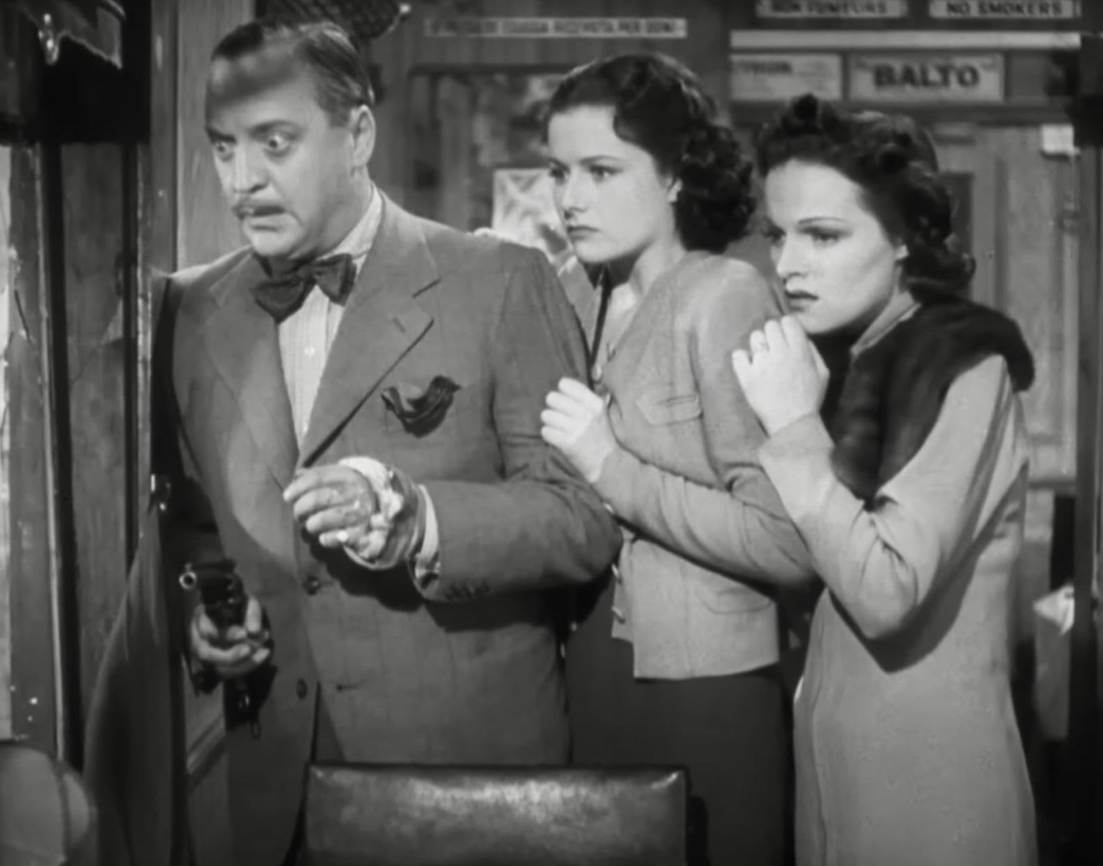 Best Mystery Movies of All Time: 25 Picks Explained 4 Black-and-white still of a man holding a gun near a doorway, with two women close behind him, all three looking tense in a cramped interior.
