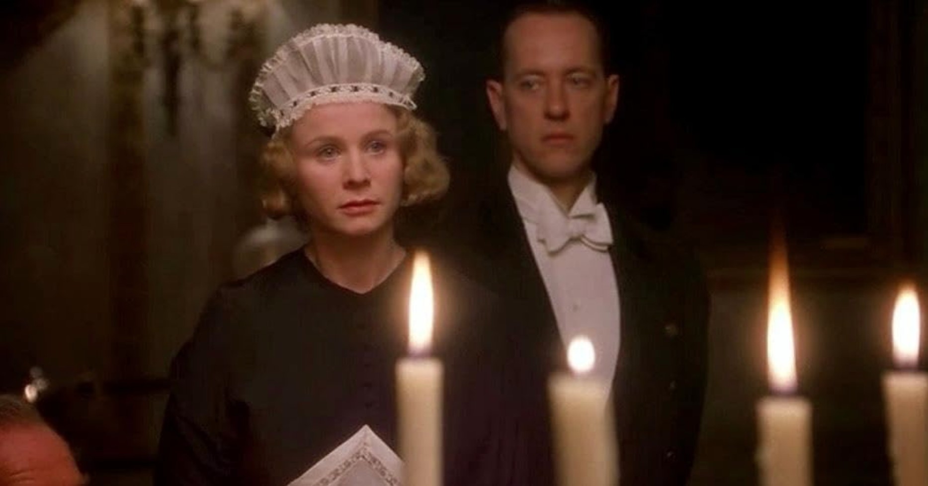 Best Mystery Movies of All Time: 25 Picks Explained 6 A maid in a white cap and dark uniform stands in a softly lit room with candles in the foreground; a man in formal evening wear stands behind her.
