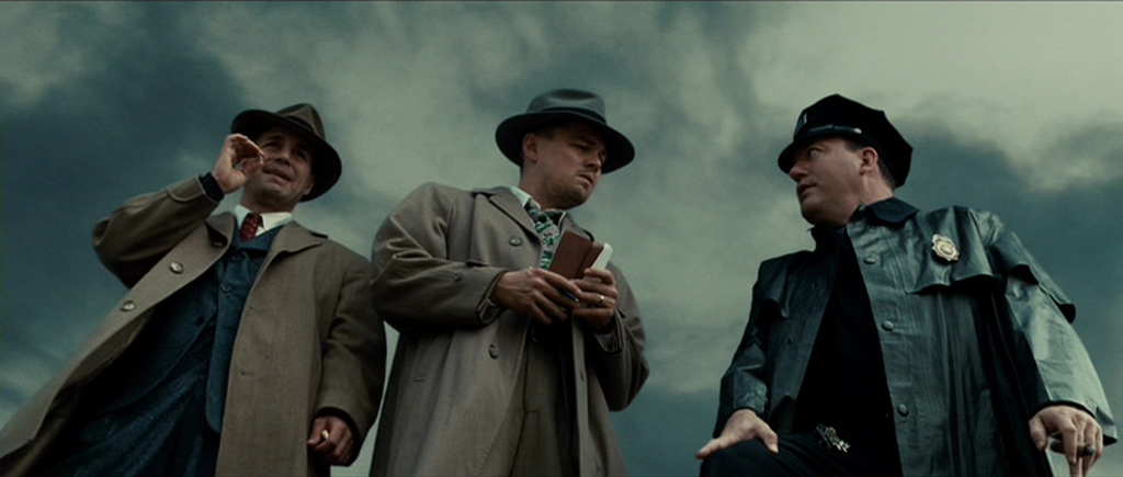 Best Mystery Movies of All Time: 25 Picks Explained 21 Three men in coats and hats stand outdoors under a cloudy sky; one wears a police uniform while another holds a notebook.