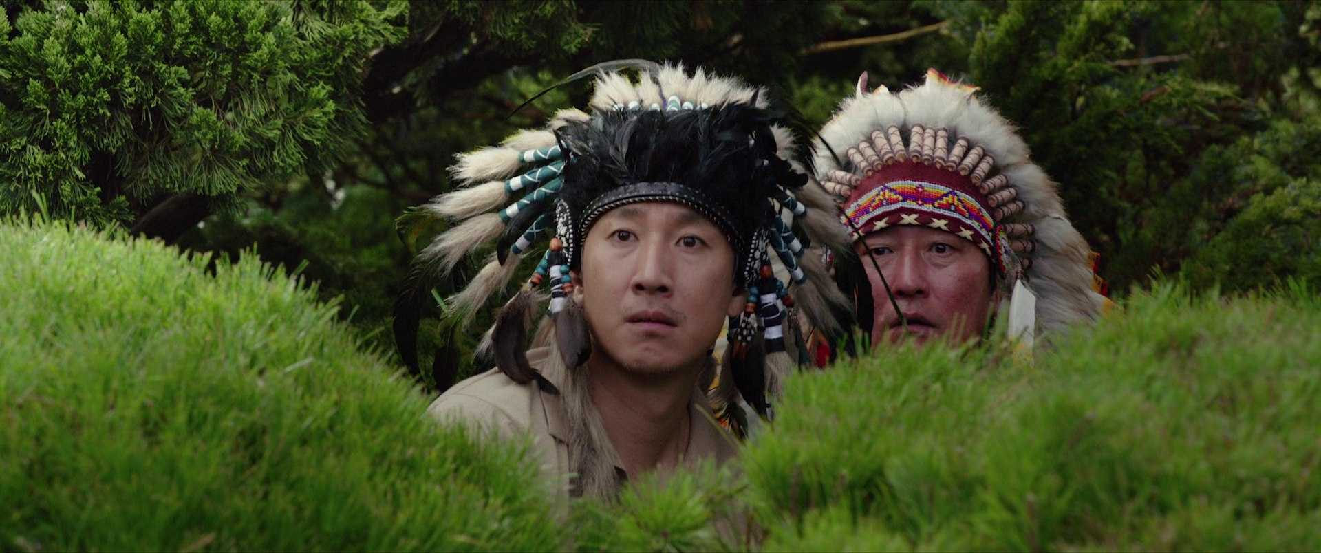 Genre Theory in Film: How Genres Organize Expectation and Meaning 4 Mr. Park and Ki-taek wear feathered headdresses and crouch behind bright green shrubs, staring tensely toward something happening off screen at a garden party