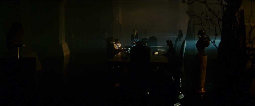 Post-Structuralism in Film Studies: A Complete Guide 3 A dark, smoky room with people seated around a table. A bright beam of light enters from the right, leaving most figures in silhouette.