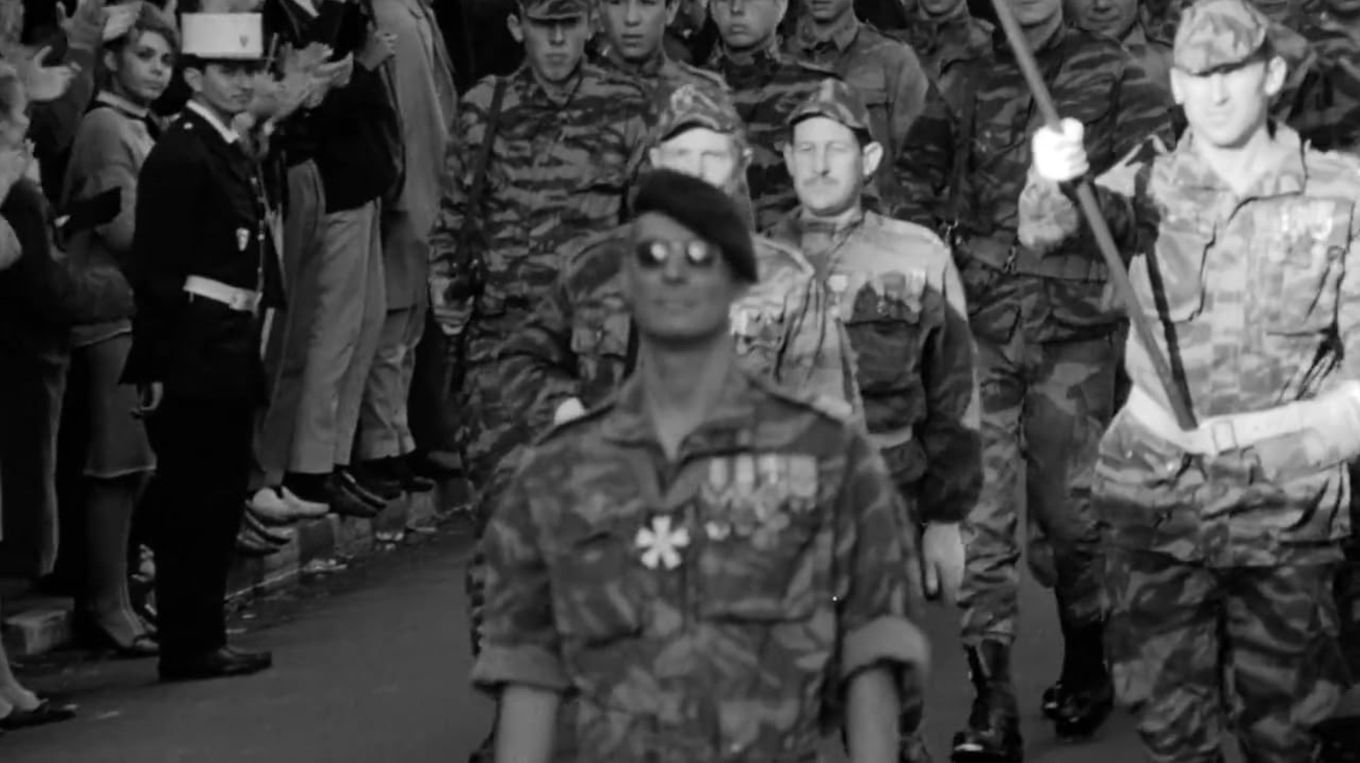 Third Cinema: Definition, Theory, and Key Examples 2 Black-and-white street scene with French soldiers in camouflage marching forward. A crowd of civilians lines the street on the left, and one soldier at the front is out of focus while others behind him are sharper.