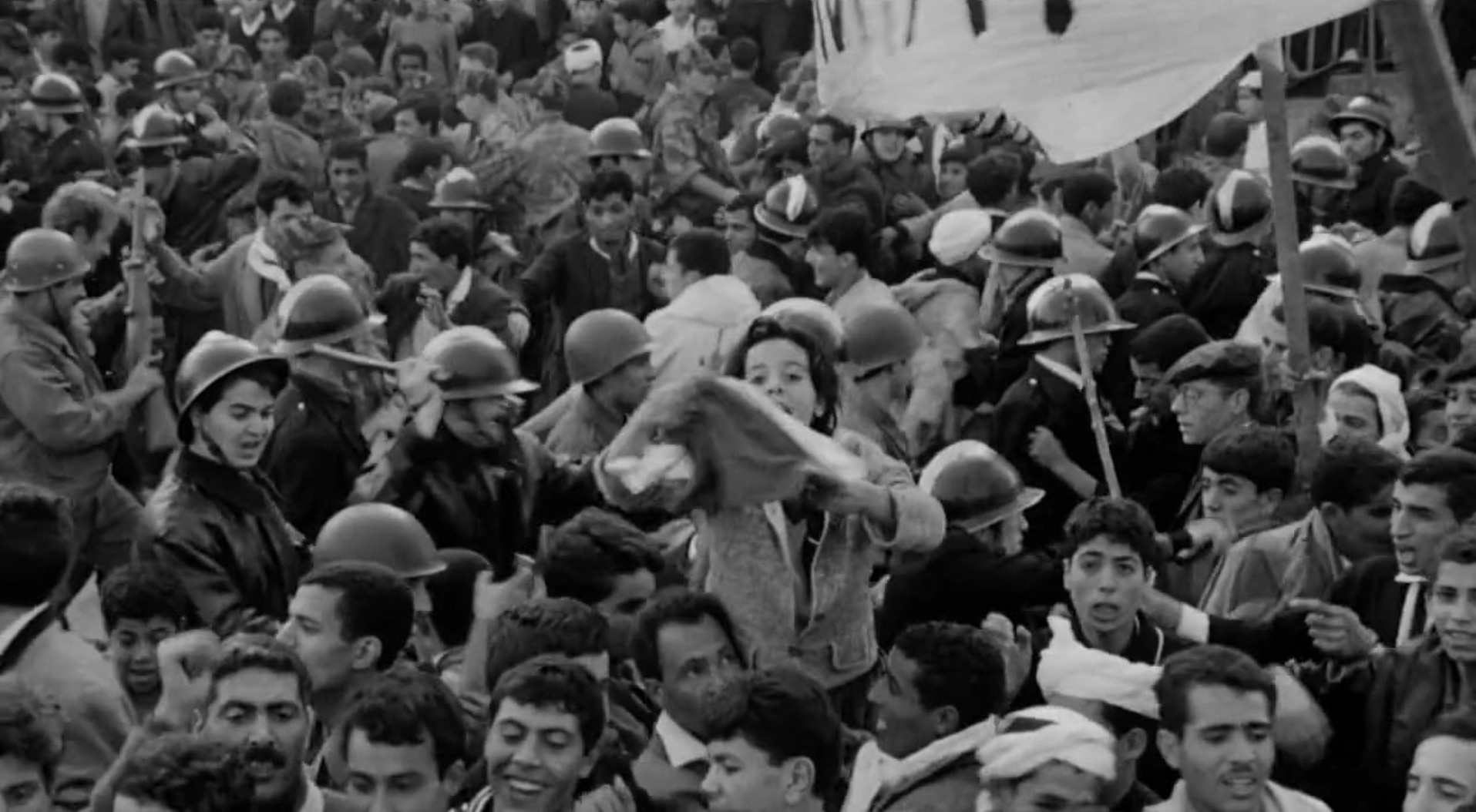 Third Cinema: Definition, Theory, and Key Examples 3 Black-and-white crowd scene with many civilians packed together while uniformed police and soldiers in helmets move through the crowd. A large banner is partially visible at the top right.